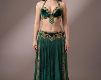 May include: A dark green velvet belly dance costume consisting of a halter-style bra top and a matching floor-length skirt. Both pieces feature intricate gold embroidery, beadwork, and long fringe accents along the waist and neckline.