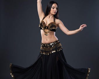 May include: A black belly dance costume consisting of a halter-style bra top and a long, flowing skirt. Both pieces are heavily embellished with gold-toned metal coins and beads that hang along the edges, creating a shimmering, layered effect.