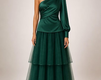 May include: A dark emerald green midi dress featuring a satin one-shoulder bodice with a long sleeve and a cuffed wrist. The waist is fitted, transitioning into a voluminous, tiered tulle skirt that falls below the knees in a layered design.