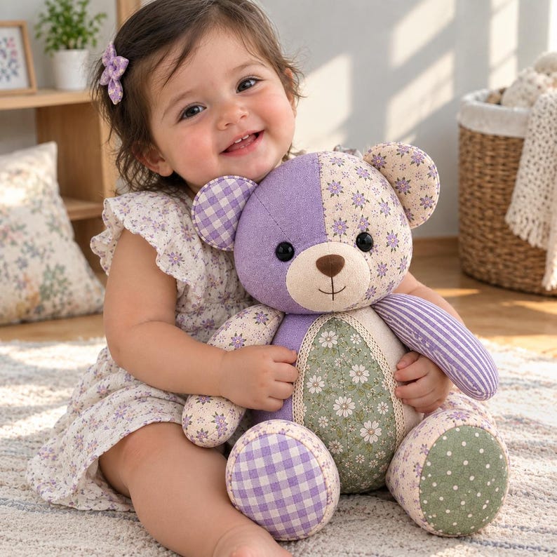 May include: A plush teddy bear constructed from various fabric patches in shades of purple, green, and white. The bear features a mix of floral, gingham, striped, and polka dot patterns, with black button eyes and a stitched brown nose and mouth.