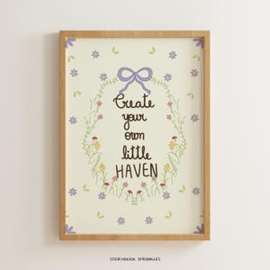 Pode incluir: Uma impressão de arte emoldurada com fundo creme claro e uma coroa oval central de caules verdes, pequenas flores coloridas e um laço lavanda no topo. O texto diz Create your own little HAVEN em letras cursivas de cor castanho escuro.