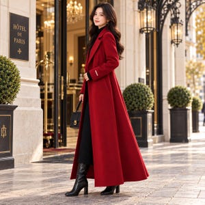 May include: A long, floor-length red wool coat with a structured collar, long sleeves, and a single-breasted front. The coat is worn over a black outfit, paired with black leather boots and a small black handbag with a gold-toned clasp.