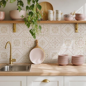 Könnte beinhalten: Eine Küche mit einem Messingwasserhahn, einem Edelstahlspülbecken und einer Arbeitsplatte aus Holz. Ein Regal darüber enthält rosa Schüsseln, ein Holzschneidebrett, weiße Krüge und eine Schüssel mit Leopardenmuster. Die Wand hat florale Fliesen.