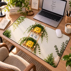 Puede incluir: Una alfombrilla de escritorio rectangular con fondo crema claro y un diseño impreso de dos macetas amarillas con caras sonrientes colgadas de cuerdas. Las macetas contienen enredaderas verdes y tienen piernas colgantes con zapatillas deportivas.