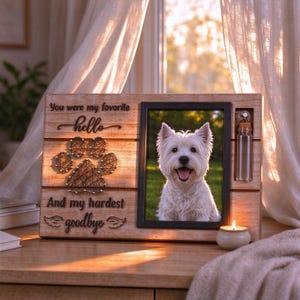 May include: A light-colored wooden memorial plaque featuring a black frame with a photo of a white dog, a black string art paw print, and the text "You were my favorite hello And my hardest goodbye" with a small glass vial attached.