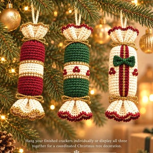May include: Three cylindrical crochet ornaments shaped like Christmas crackers, featuring cream, red, and green yarn with gold cord accents. Each piece has ruffled ends and is suspended by a loop. The text reads: Hang your finished crackers individually or display all three together for a coordinated Christmas tree decoration.