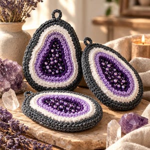 May include: Three crocheted geode-inspired ornaments featuring dark gray outer borders, white middle rings, and light purple inner sections filled with dark purple beads. Each piece has a small crocheted loop at the top for hanging purposes.