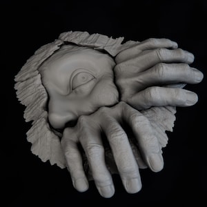 May include: A grey monochromatic wall sculpture depicting a single eye and two hands emerging from a textured, torn-paper-like surface. The hands are positioned as if gripping the edges of the opening, with detailed skin texture and visible knuckles.