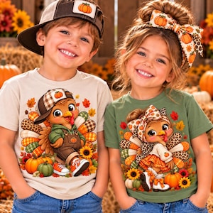 May include: A beige t-shirt featuring a cartoon turkey wearing a baseball cap and overalls, and a green t-shirt featuring a cartoon turkey wearing a large hair bow. Both shirts display autumn-themed graphics with pumpkins, sunflowers, and fall leaves.