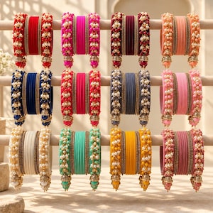 May include: A collection of twelve sets of bangles arranged in a grid. Each set features a central group of solid-coloured velvet bangles flanked by two decorative beaded bangles with small dangling charms in matching colours and metallic accents.