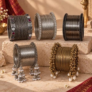 Könnte beinhalten: Fünf Sets aus Metallarmreifen. Das Set oben links besteht aus dunklen, texturierten Bändern mit roten und klaren Steinen. Das Set oben in der Mitte hat silberne Bänder mit klaren Steinen. Das Set oben rechts hat dunkle Bänder mit schwarzen Steinen. Die unteren Sets bestehen aus silbernen und goldenen Bändern mit baumelnden weißen Perlenanhängern.