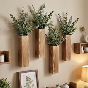 May include: Four rectangular wooden wall planters with a natural grain finish, each holding a lush arrangement of green eucalyptus stems. The planters are mounted vertically on a plain wall, creating a uniform display of greenery and wood.