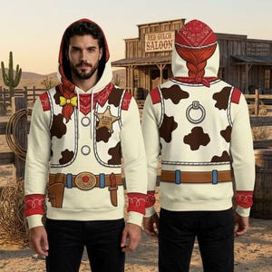 May include: A long-sleeve hoodie featuring a cowgirl-inspired print with a cream base, brown cow spots, a red bandana collar, a yellow bow, and a gold sheriff badge labeled Jessie. The back displays a matching cow print and a silver ring detail.