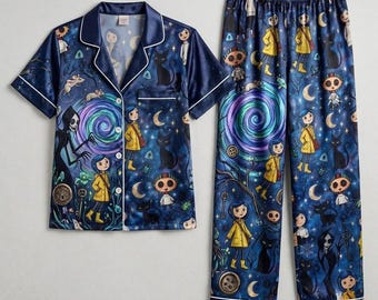 May include: A two-piece pajama set featuring a short-sleeved button-down shirt and matching pants. The fabric is dark blue with a repeating print of characters, black cats, mice, keys, buttons, moons, and swirling purple and blue vortexes.