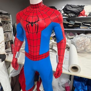 May include: A full-body Spider-Man costume featuring a vibrant red and blue color scheme. The red sections on the chest and arms display a black web pattern, with a prominent black spider emblem centered on the chest. The suit has a high neck.