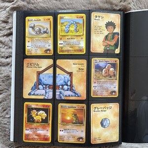 May include: A black plastic trading card binder page containing nine Pokémon cards, including Brock's Geodude, Onix, Brock's Dugtrio, Vulpix, and Brock's Sandshrew, alongside cards featuring Brock, Pewter City Gym, and the Boulder Badge.