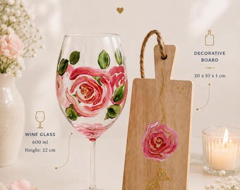 May include: A gift set featuring a 600 ml wine glass with a height of 22 cm and a decorative wooden board measuring 20 x 10 x 1 cm. Both items are hand-painted with pink rose motifs and green leaves. The text reads Perfect Gift Set PINK MAGIC.