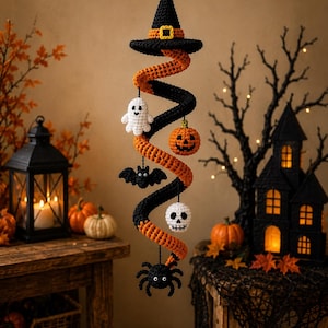 Könnte beinhalten: Eine hängende Halloween-Dekoration aus Häkelarbeit mit einem schwarzen Hexenhut an der Spitze, gefolgt von einem spiralförmigen orange-schwarzen Körper. An der Spirale sind kleine gehäkelte Figuren befestigt, darunter ein weißes Gespenst, ein orangefarbener Kürbis, eine schwarze Fledermaus, ein weißer Totenkopf und eine schwarze Spinne.