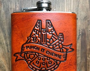 May include: A brown leather flask with a silver top and a black engraved image of the Millennium Falcon with the text "Punch it Chewie".