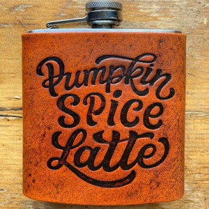 Könnte beinhalten: Eine braune Lederflasche mit silbernem Verschluss und dem eingravierten Text "Pumpkin Spice Latte" auf der Vorderseite.