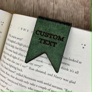 May include: A green leather bookmark with the text "CUSTOM TEXT" engraved on it. The bookmark is in the shape of a flag.