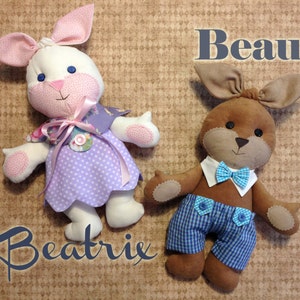 May include: Two handmade plush bunny toys, one white with a purple dress and pink accents, the other brown with blue and white checkered pants and a blue bow tie. The white bunny is named Beatrix and the brown bunny is named Beau.