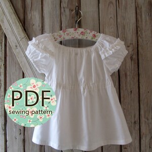 May include: White peasant style top with ruffled sleeves and a gathered waist. The top is hanging on a floral patterned hanger. The text "PDF sewing pattern" is on a circle with a floral design.