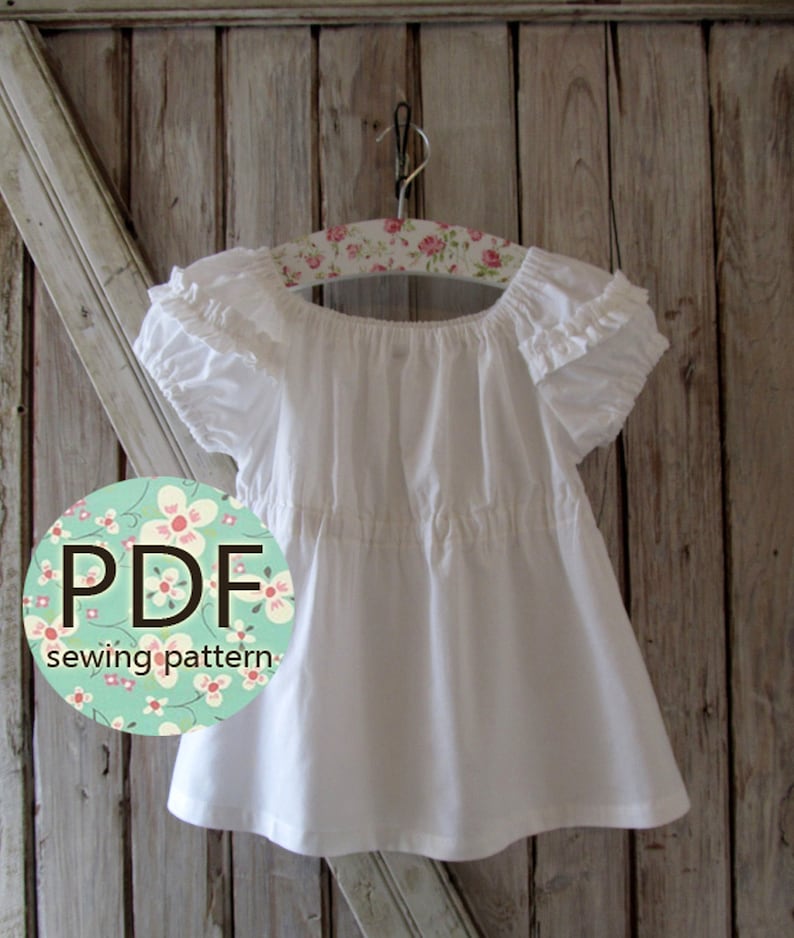 May include: White peasant style top with ruffled sleeves and a gathered waist. The top is hanging on a floral patterned hanger. The text "PDF sewing pattern" is on a circle with a floral design.