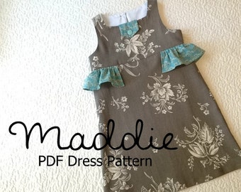 May include: A gray sleeveless dress with a white floral pattern and a blue ruffle trim. The dress has a button closure at the neckline and the text "Maddie PDF Dress Pattern" is printed below the dress.