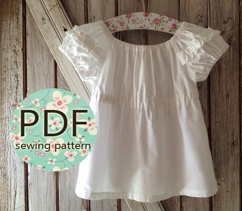 May include: A white cotton peasant top with a gathered neckline and ruffled sleeves. The top is hanging on a floral hanger and has a circle with the text "PDF sewing pattern" on it.