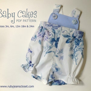 May include: A white and blue floral print baby romper with a blue and white gingham bib and two buttons. The romper has a ruffled hem and is available in sizes 3m, 6m, 12m, 18m, and 24m. The text "Baby Cakes PDF Pattern" is at the top of the image.