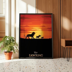 Op de afbeelding: Een ingelijste rechthoekige wandkunstprint met een silhouet van een leeuw, een wrattenzwijn en een stokstaartje die tegen een levendige oranje en rode zonsondergang aanlopen. De tekst "Disney THE LION KING" staat in goud onderaan de print.