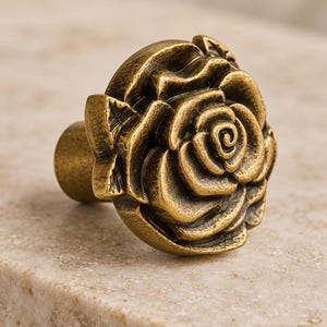 Può includere: Un pomello per cassetto a forma di rosa in fiore con una finitura in ottone antico scuro. La ferramenta in metallo presenta petali dettagliati e sovrapposti e una base cilindrica, con una superficie metallica testurizzata e usurata.