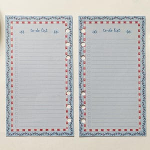 Peut inclure: Deux feuilles de planning bleu clair avec un en-tête to-do list, des lignes et des colonnes de cases à cocher. La bordure présente un motif à carreaux rouges et blancs entouré d'une vigne bleue. Chaque page a six trous circulaires.