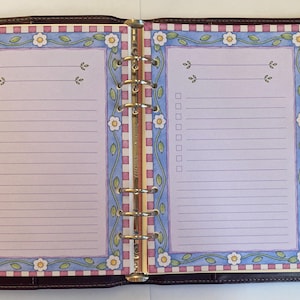 May include: A dark brown leather six-ring binder open to two pages of stationery. The pages feature a light purple center with a border of pink and white checkered squares, blue vines, and white flowers, including lined sections and checkboxes.