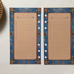 Può includere: Due inserti rettangolari per agenda con un centro color marrone chiaro caratterizzato da linee orizzontali e una colonna verticale di caselle di controllo. I bordi sono decorati con un motivo floreale blu con girasoli arancioni e viticci.