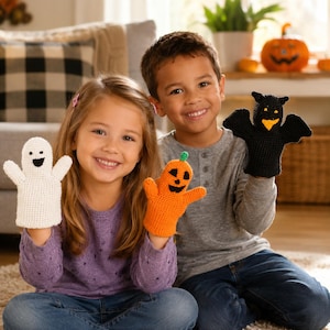 May include: Three crocheted finger puppets featuring a white ghost with a black face, an orange pumpkin with a black jack-o'-lantern face, and a black bat with yellow eyes and a yellow beak, all crafted with detailed yarn stitching.