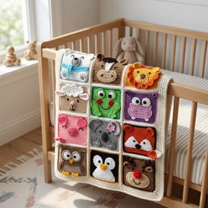 Op de afbeelding: Een crèmekleurige gehaakte babydeken met twaalf vierkante panelen, elk met een ander dierengezicht, waaronder een ijsbeer, paard, leeuw, schaap, kikker, nijlpaard, varken, koala, vos, uil, pinguïn en rendier in verschillende kleuren.