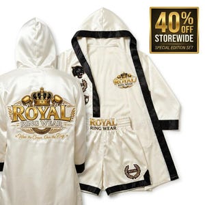 Pode incluir: Um conjunto de boxe em cetim branco composto por um roupão e calções a condizer com acabamento em preto. O roupão apresenta um grande logótipo de coroa bordado a ouro nas costas com o texto ROYAL RING WEAR e Wear the Crown. Own the Ring.