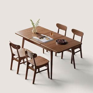 Op de afbeelding: Een rechthoekige houten eettafel met vier bijpassende stoelen. De tafel heeft een warme bruine houtnerfafwerking en is voorzien van een open boek, een glazen vaas met witte bloemen, een klein glas en een donkere kom gevuld met rode kersen.