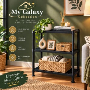 May include: A black three-tier shelving unit featuring a grid-patterned surface on each shelf. The unit is decorated with a potted plant, a white ceramic vase, a framed picture, two books, and two woven baskets containing folded textiles.