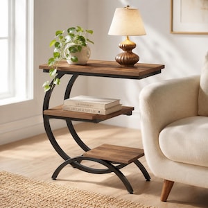 May include: A C-shaped side table with a dark wood grain finish and a black metal frame. The table features three tiered shelves, a beige fabric lamp with a brown base, a white potted plant, and two books titled The Kinfolk and Live Beautifully.