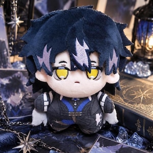 May include: A plush doll featuring dark blue hair with light purple highlights, bright yellow eyes, and a pale complexion. The doll wears a dark blue and black outfit with intricate detailing, including a blue chest panel and white accents.