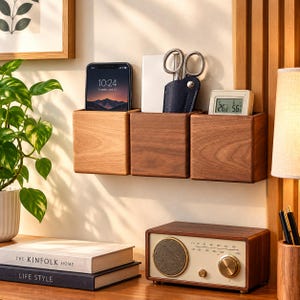 May include: Three square wooden wall-mounted storage boxes in varying wood tones. The left box holds a smartphone, the center box contains scissors in a dark blue sheath, and the right box holds a digital thermometer displaying 26.8 degrees and 56 percent.