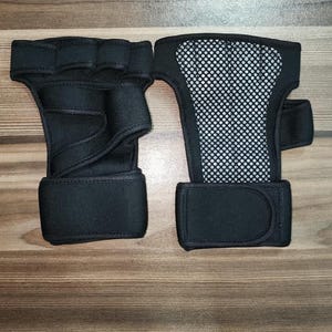 May include: A pair of black fingerless hand supports featuring a wrap-around wrist strap with a hook-and-loop closure. One support shows the palm side with a textured grip, while the other displays the back side with a breathable mesh panel.