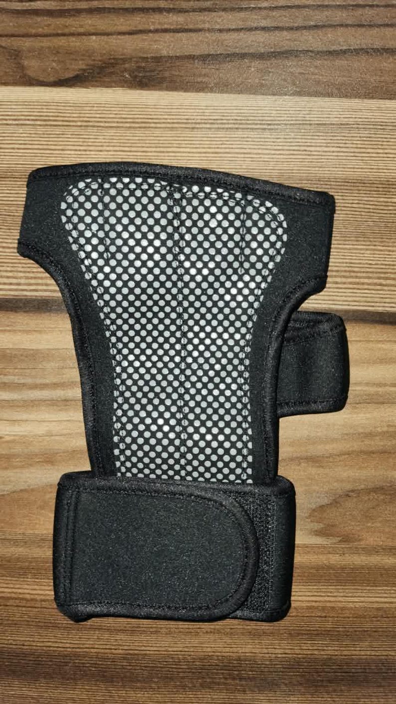 May include: A black wrist support brace featuring a central panel with a white perforated mesh pattern. The brace includes a wide adjustable strap at the base and a smaller side strap, both secured with hook-and-loop fasteners for a snug fit.