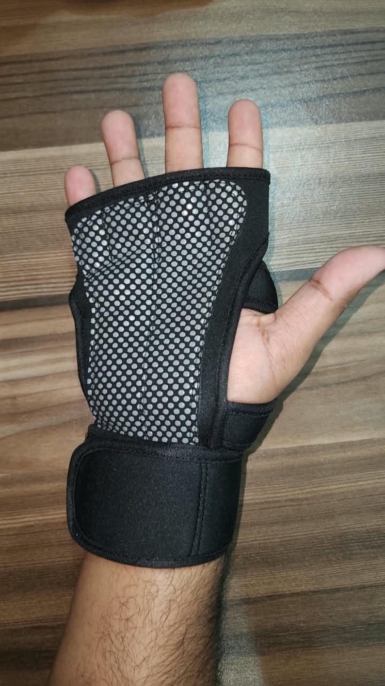 May include: A black fingerless glove with a grey mesh palm pad featuring a circular dot pattern. The glove includes a wide black wrist strap with a hook-and-loop closure, designed to provide support and grip for various physical activities.