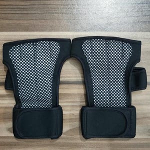May include: A pair of black wrist supports featuring a central panel of grey mesh fabric. Each support includes a wide, solid black adjustable strap at the base with a hook-and-loop closure system, designed to provide stability and support for the wrist.