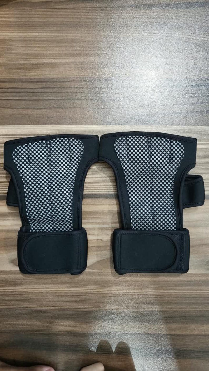 May include: A pair of black wrist supports featuring a central panel of grey mesh fabric. Each support includes a wide, solid black adjustable strap at the base with a hook-and-loop closure system, designed to provide stability and support for the wrist.