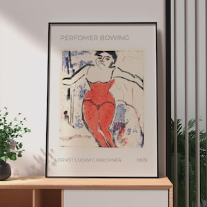 May include: A framed art print titled PERFOMER BOWING by Ernst Ludwig Kirchner 1909. The print features a stylised illustration of a figure in a red bodysuit with black outlines against a cream background with blue and red abstract accents.